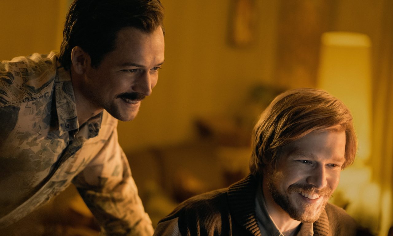 Sepia tone of Rogers looking at a computer screen over Pajitnov's shoulder; both men are smiling